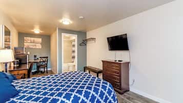 A bedroom with a bed, dresser, TV, desk, chair, and a bathroom visible through an open door.