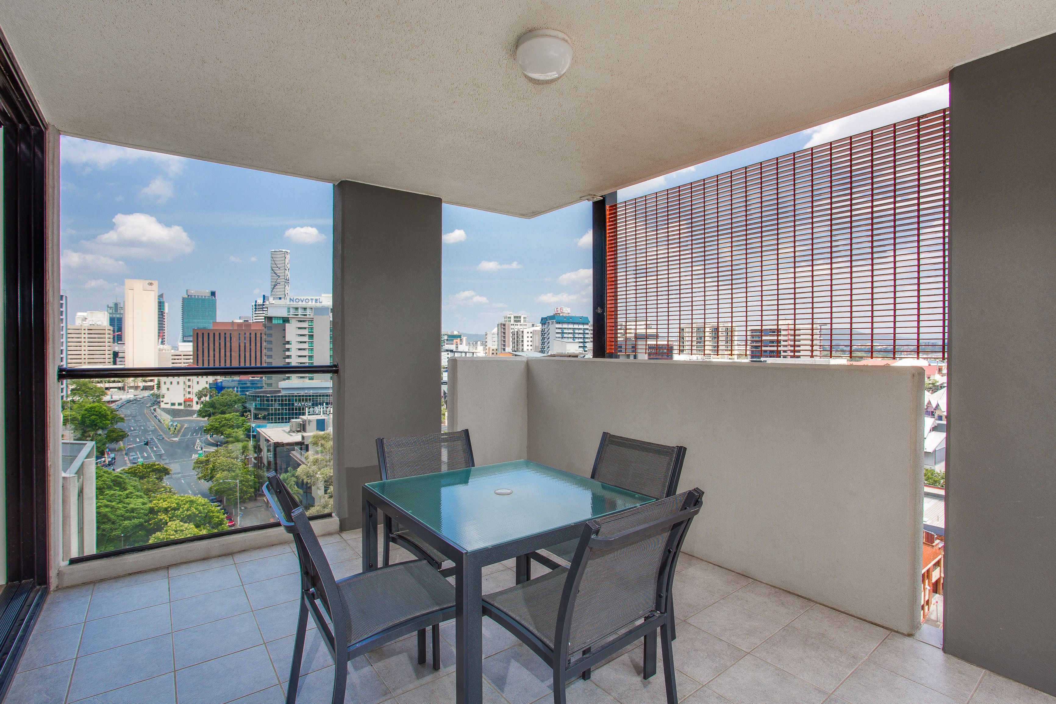A balcony with a glass table and chairs, offering a city view.