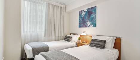 A hotel room with two beds, a ceiling fan, a painting on the wall, and a window with curtains.