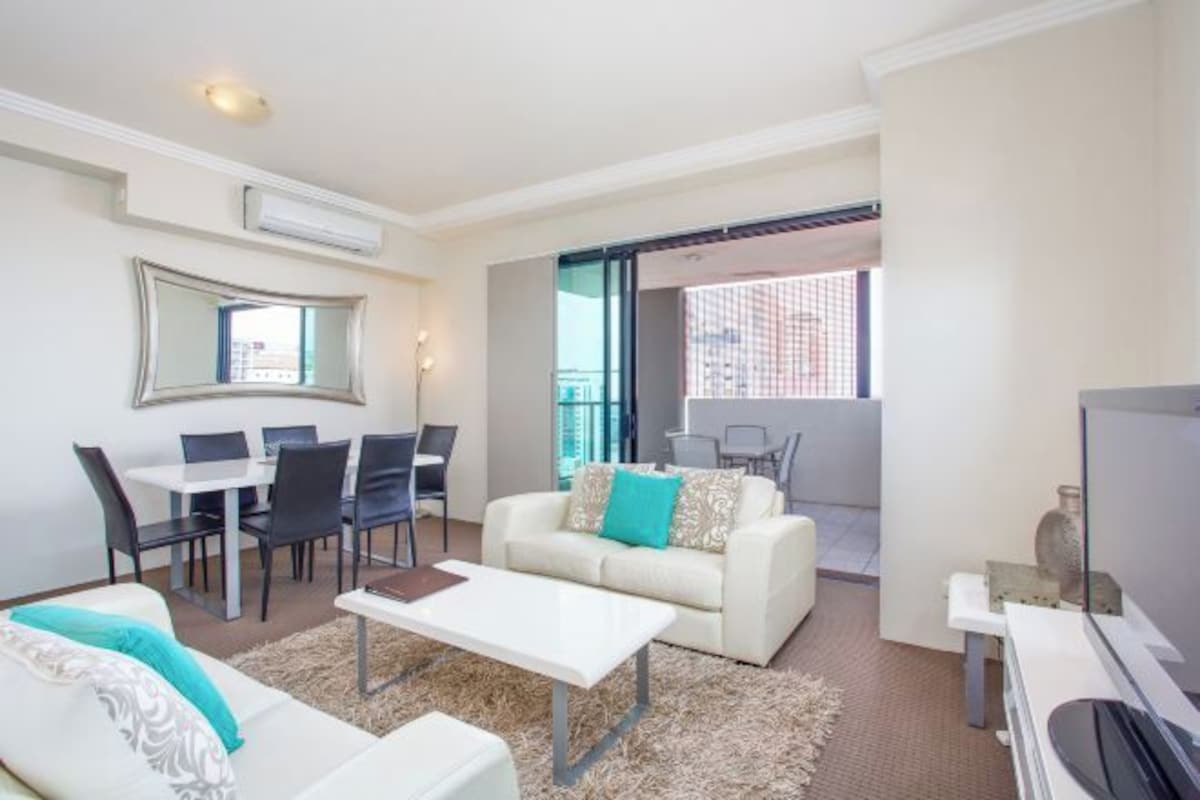 Una sala de estar moderna con un sofá blanco, una mesa de comedor con sillas, una mesa de centro y un televisor.