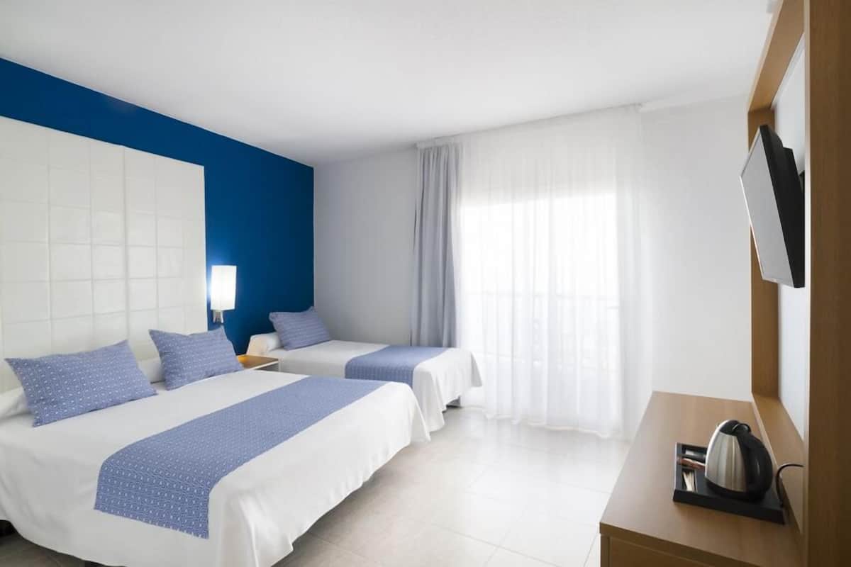 Une chambre d’hôtel avec deux lits, un bureau en bois, une bouilloire et une télévision.