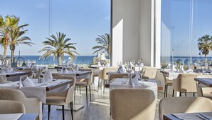 Een restaurant met gedekte tafels, met uitzicht op een strand met palmbomen en de zee.