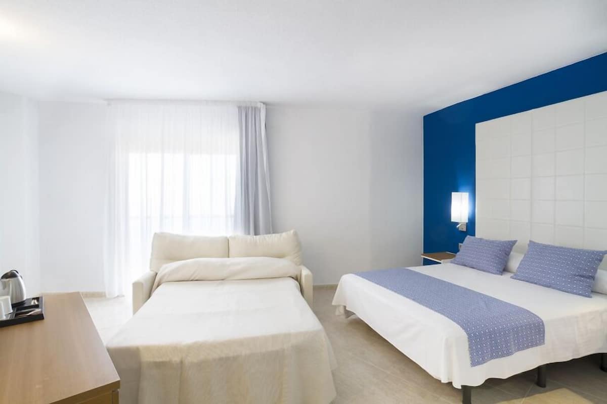 Une chambre d’hôtel avec deux lits, un bureau et une fenêtre avec des rideaux.