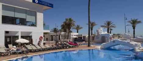 A hotel pool area with lounge chairs, a lifeguard stand, and palm trees.