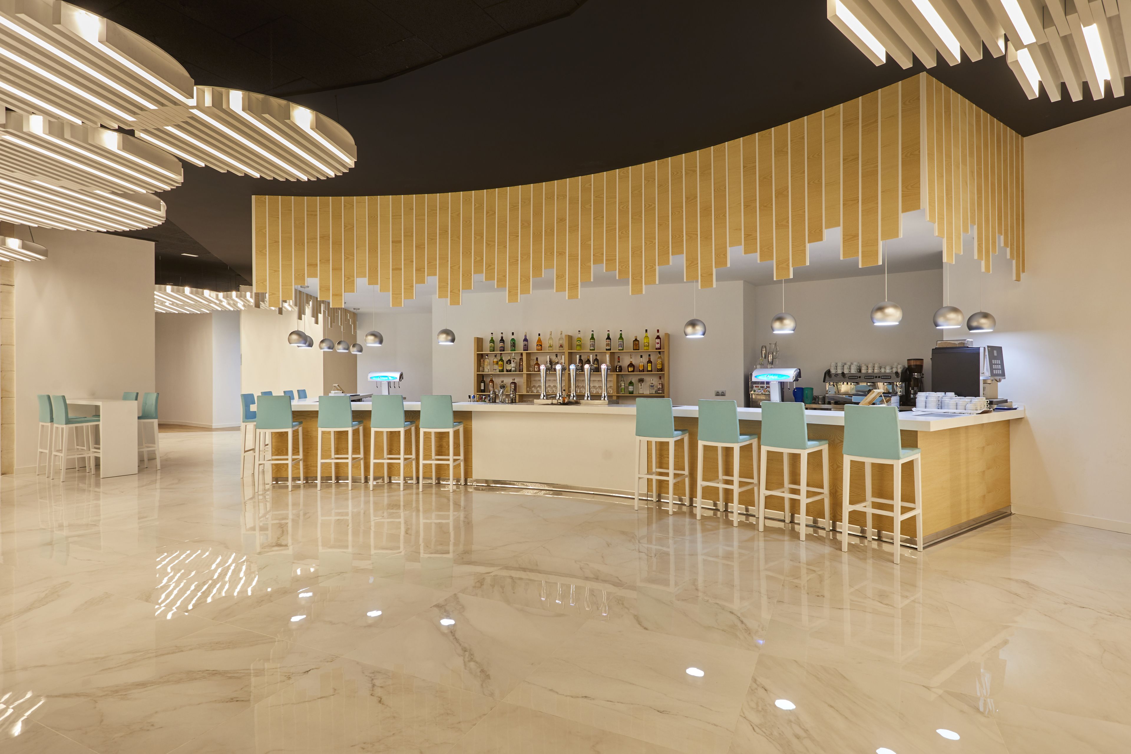 A modern bar area with a curved counter, bar stools, and pendant lighting.