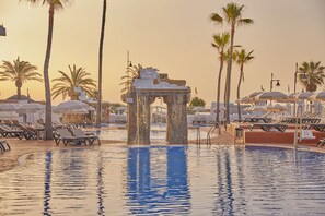 Ein Poolbereich mit Liegestühlen, Palmen und einem Wasserspiel.