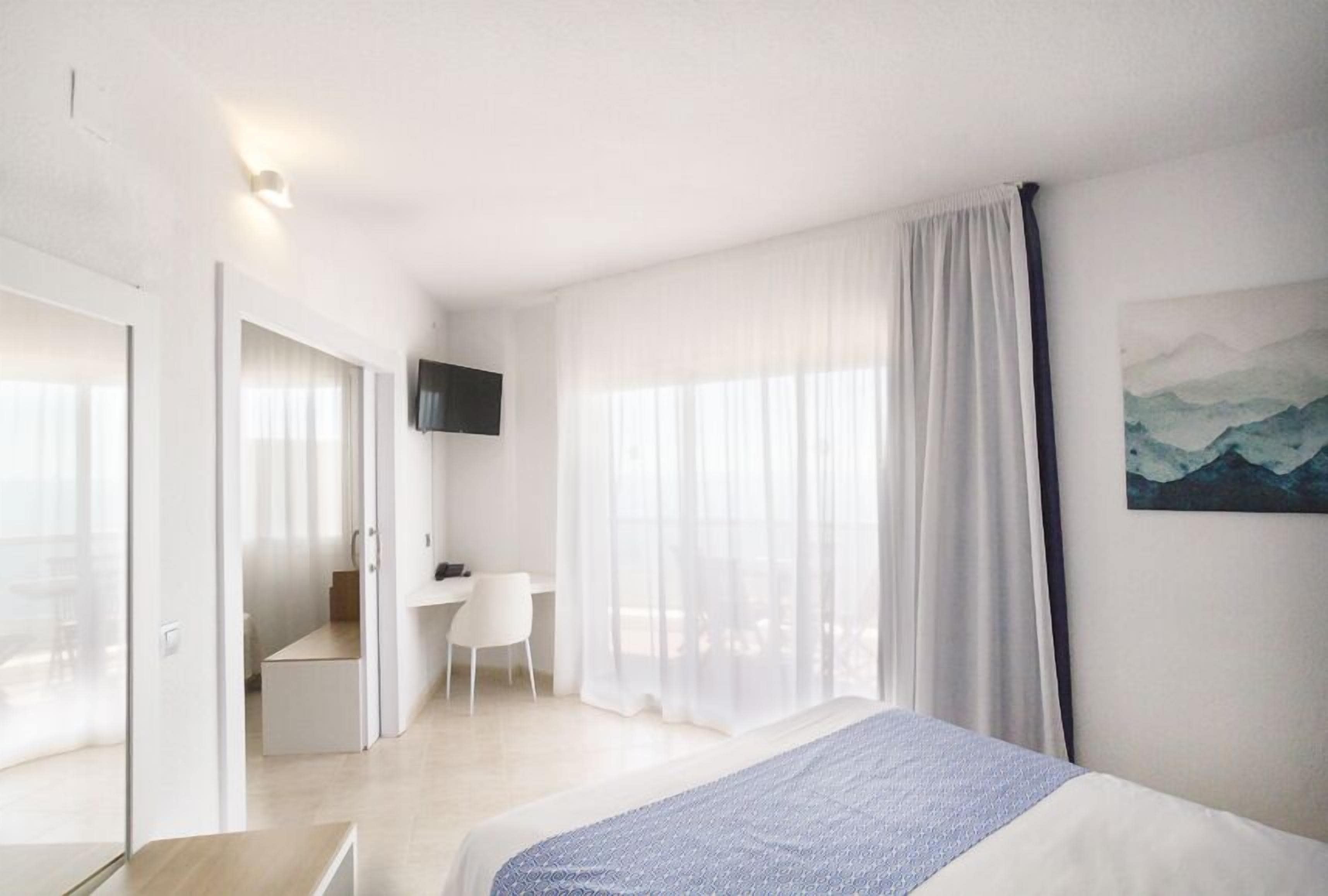 A modern hotel room with a bed, a desk, and a chair. There is a TV mounted on the wall and a painting on the wall.