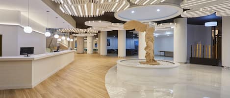 A modern hotel lobby with a marble floor, a reception desk, and a unique sculpture.