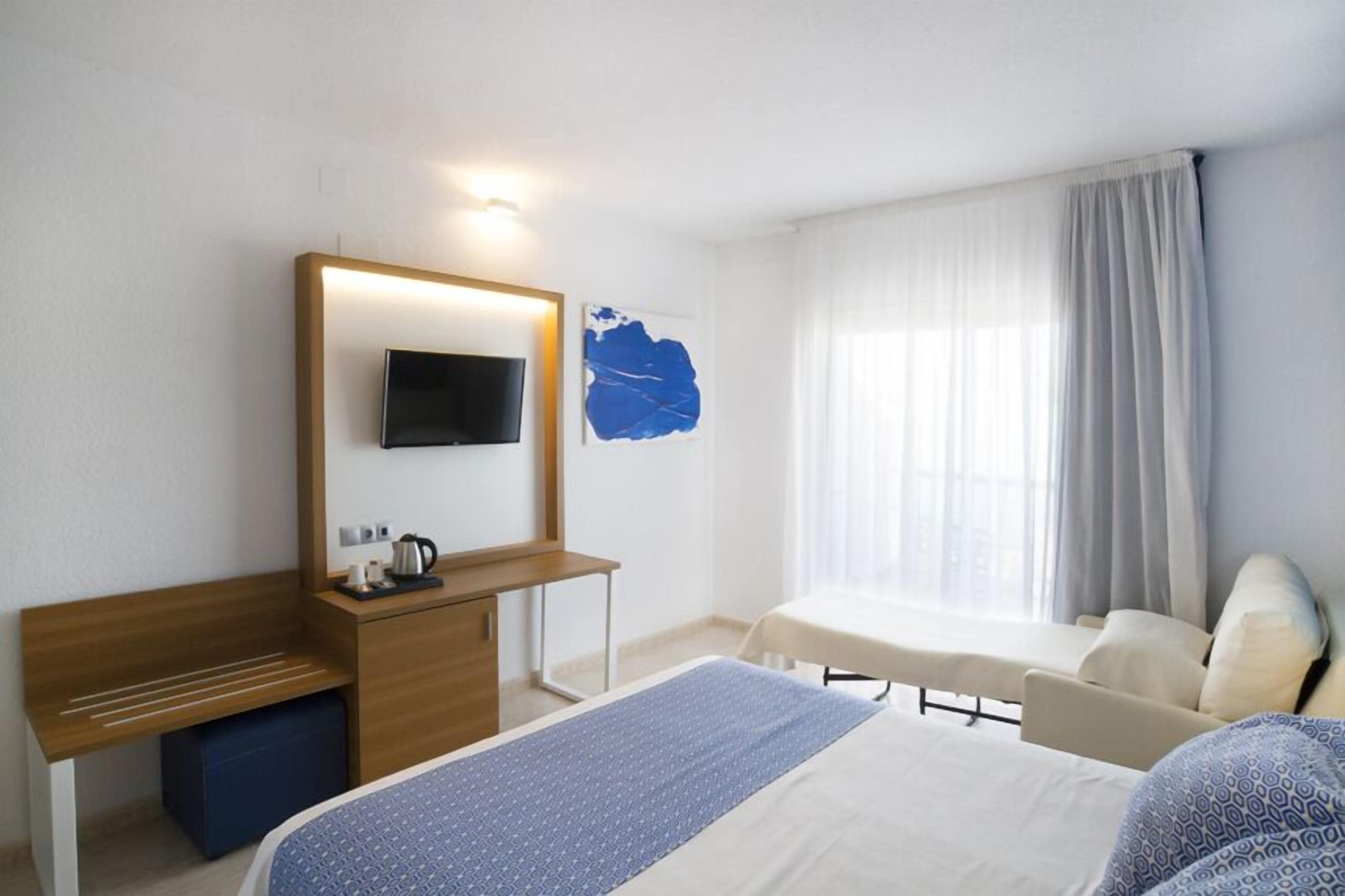 A hotel room with a bed, a desk, a chair, a TV, and a window with curtains.