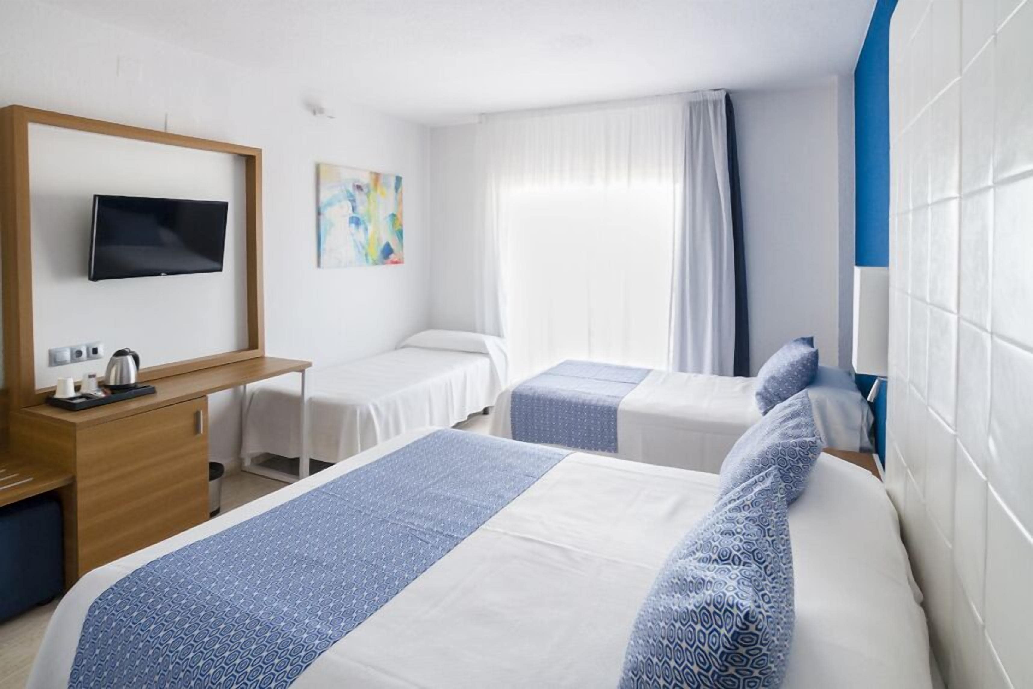 A hotel room with two beds, a desk with a television, a painting on the wall, and a window with curtains.