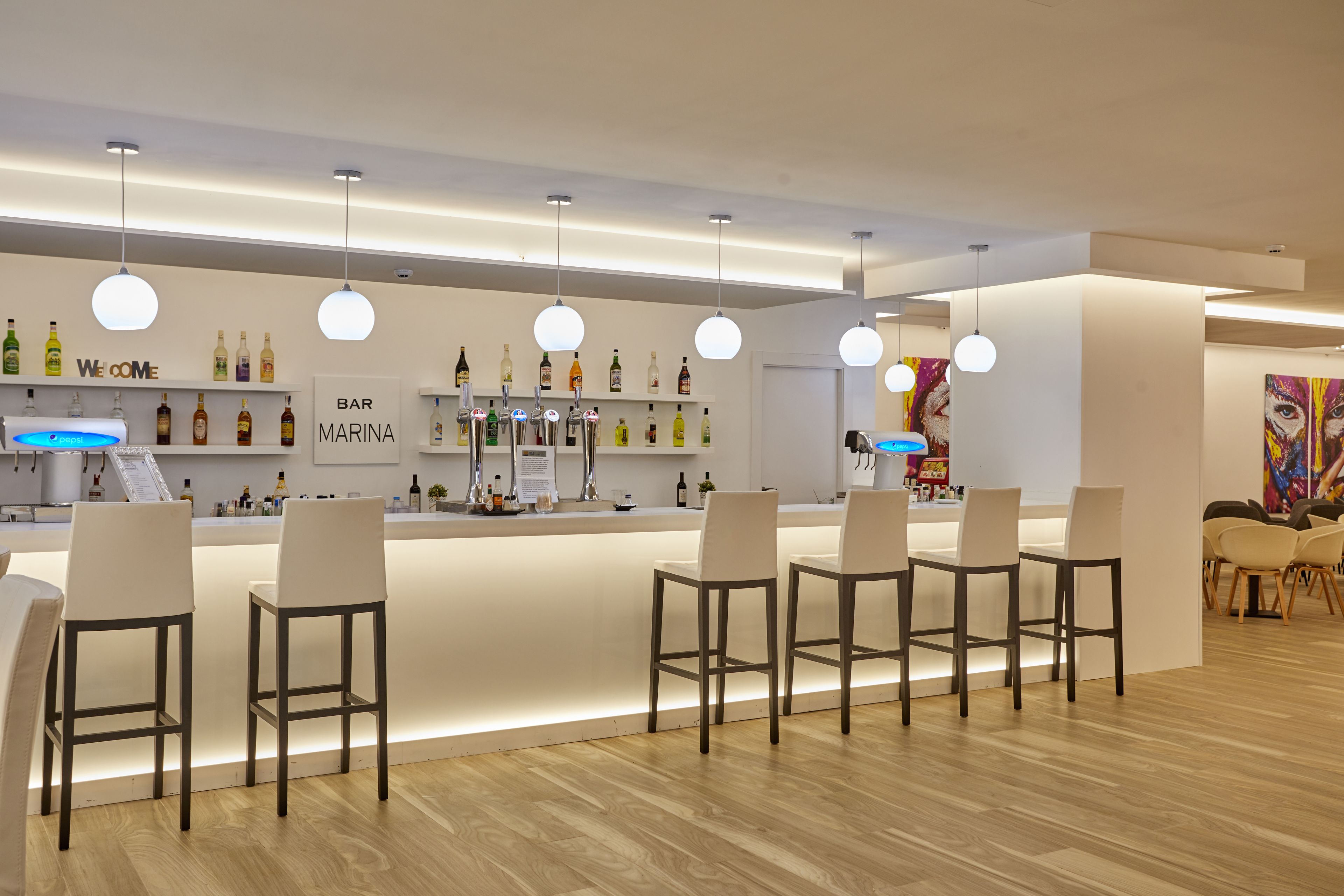 A modern bar area with a bar counter, white bar stools, and a variety of liquor bottles.