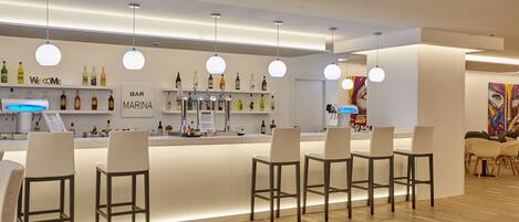 Un espace bar moderne, doté d’un comptoir, de tabourets de bar blancs et d’une variété de bouteilles d’alcool.