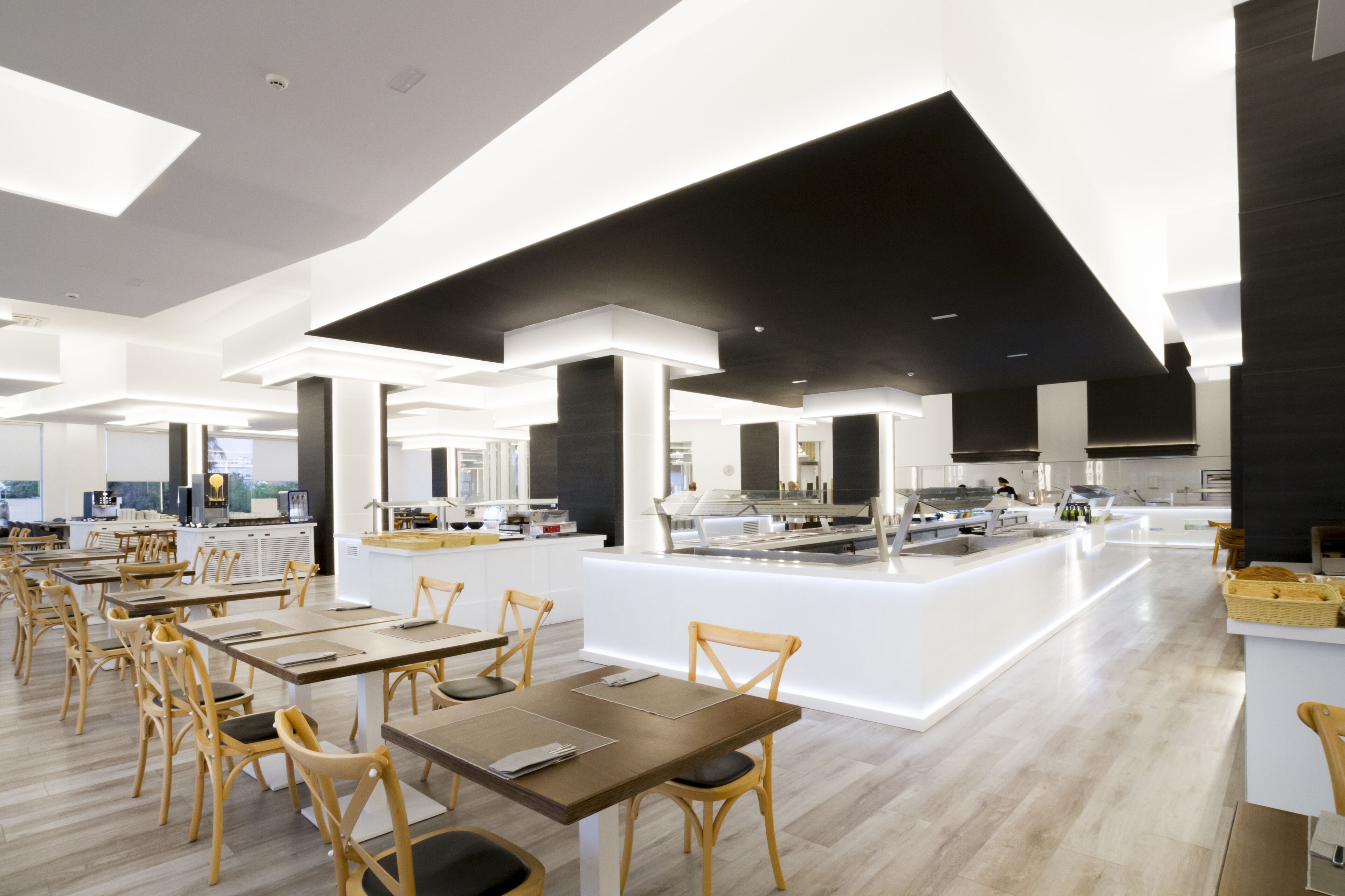 Un comedor moderno con mesas y sillas de madera, una isla central con encimera de cocina y un diseño de techo abierto y luminoso.