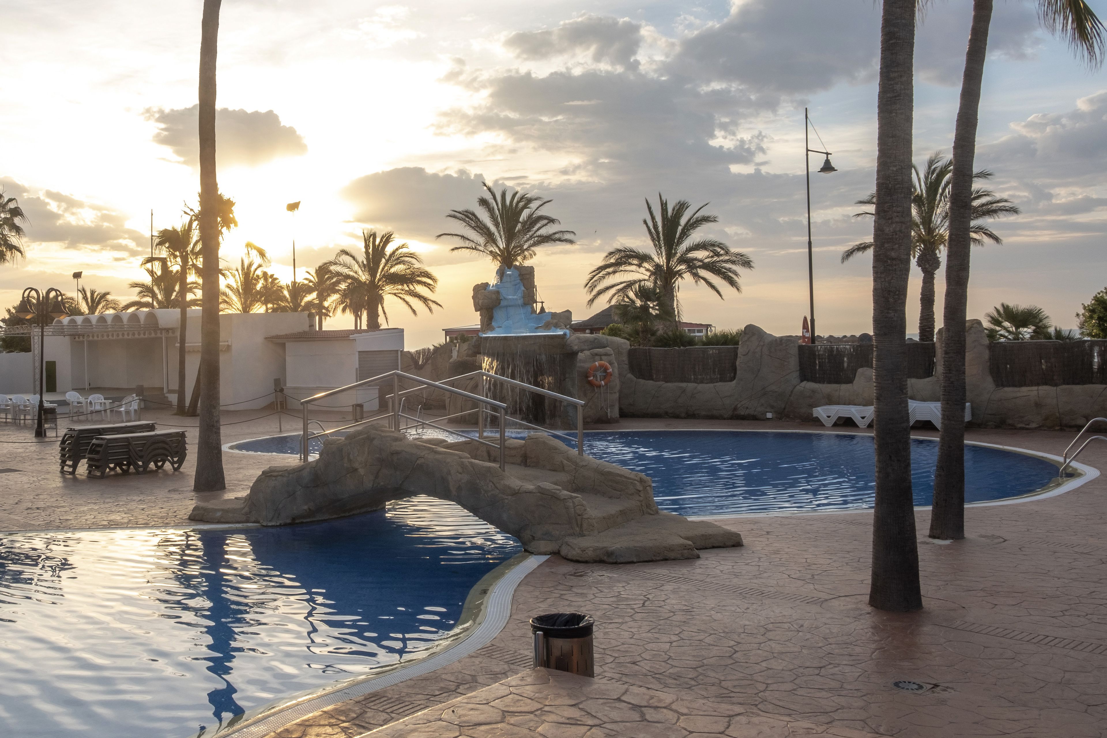 A swimming pool with a rock formation and palm trees.