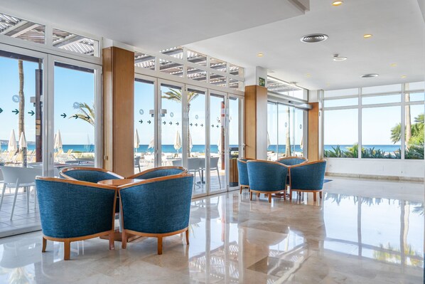 A modern hotel lobby with a glass wall offering a view of the beach and ocean. - Hotel THB El Cid - Adults Only (Palma de Mallorca)