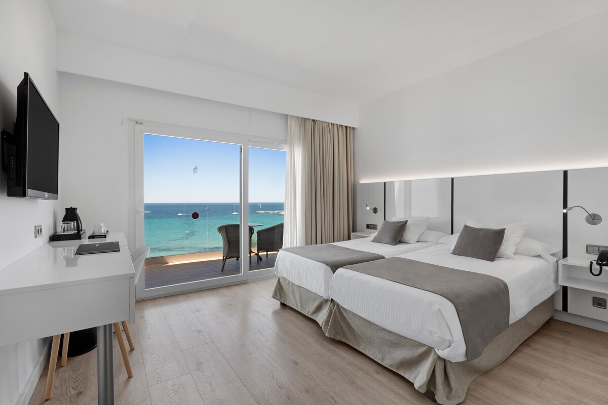 Una habitación de hotel moderna con una cama grande, un escritorio, un televisor y un balcón con vistas al mar.
