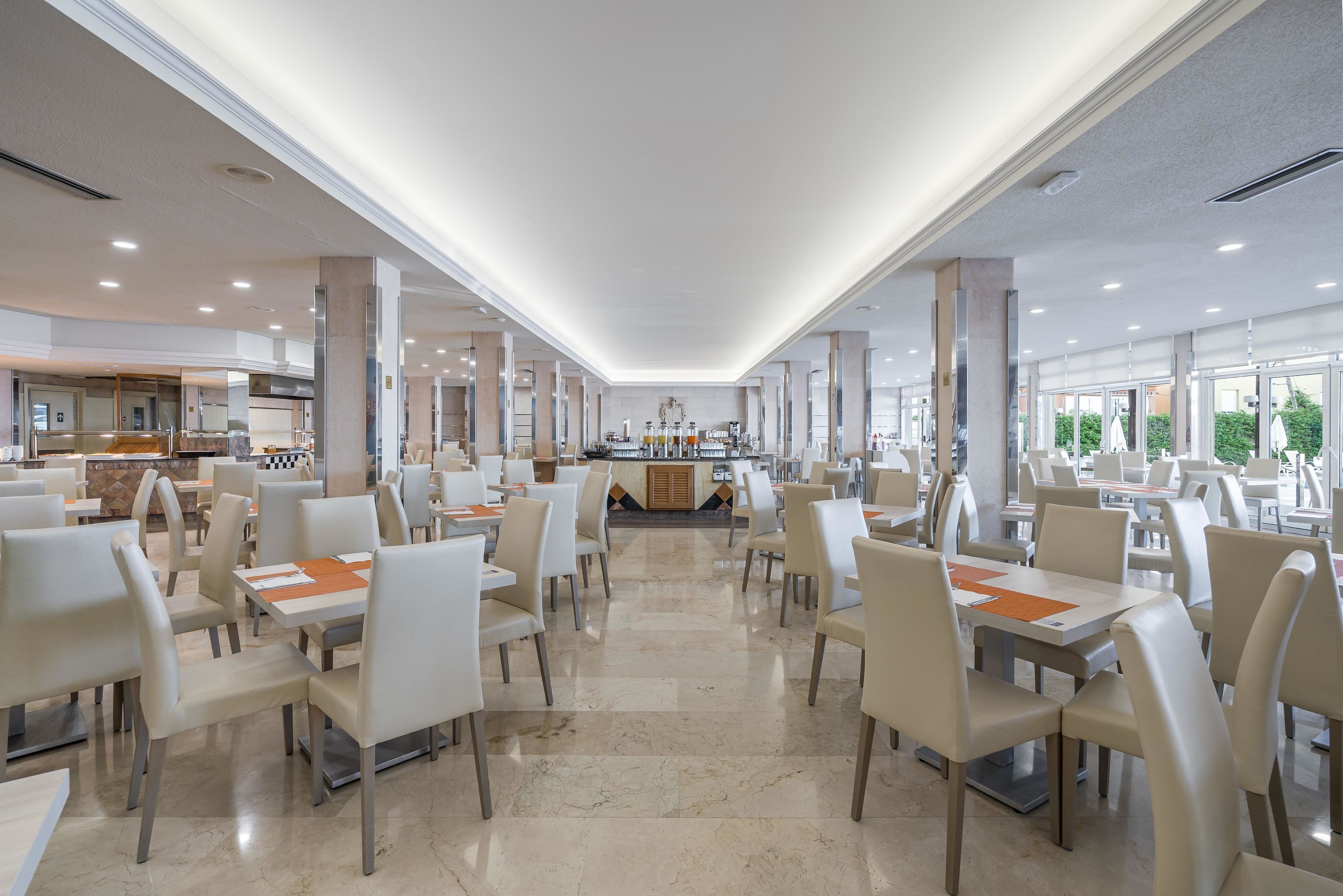 Un comedor amplio con múltiples mesas y sillas, una barra central y ventanas grandes que dejan entrar luz natural.
