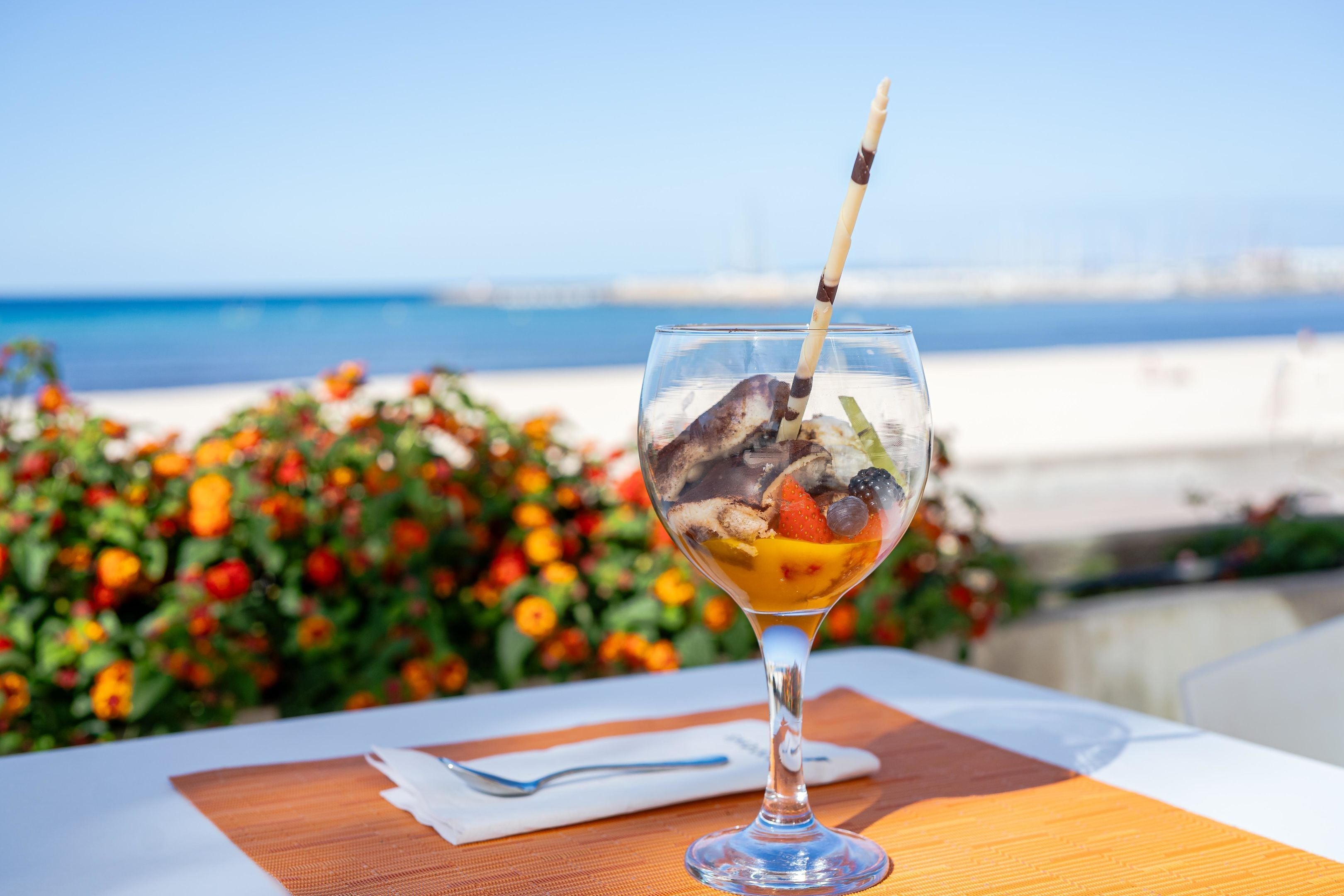 A dessert in a glass on a table with a view of the beach and ocean in the background.