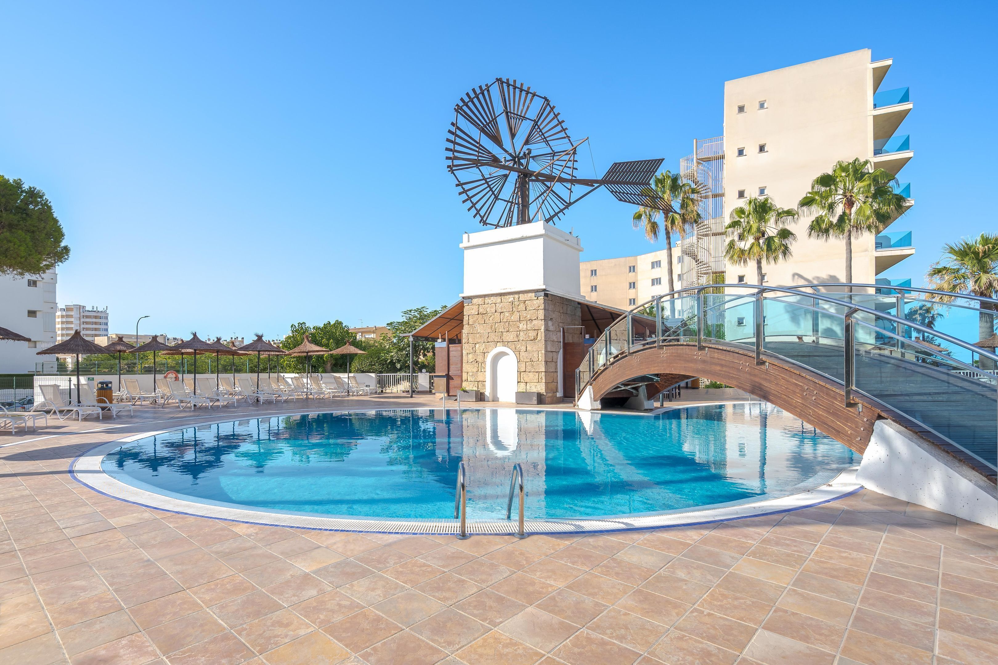 A swimming pool with a bridge, palm trees, and a windmill.