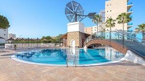 Una piscina con un puente, palmeras y un molino.