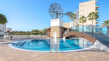 A swimming pool with a bridge, palm trees, and a windmill.