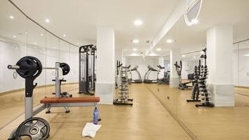 Une salle de sport moderne avec des murs recouverts de miroirs, divers appareils d’exercice et un plancher en bois.