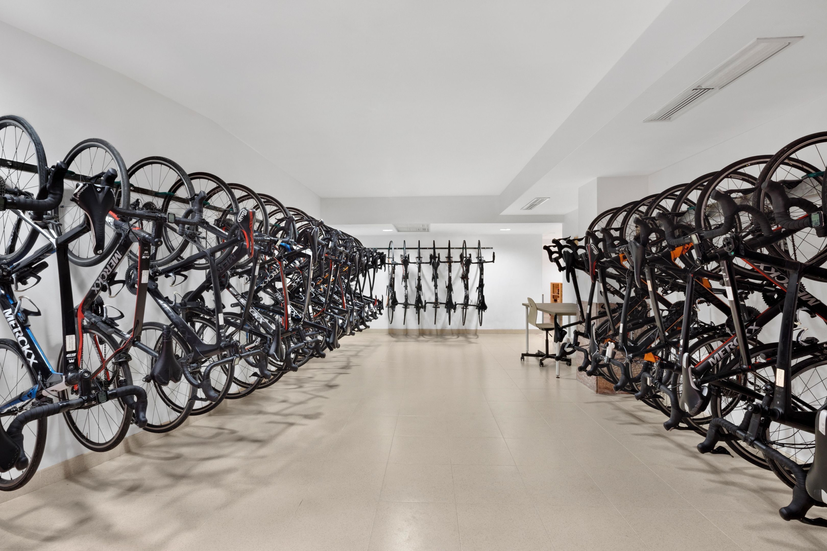 Una habitación amplia con filas de bicicletas en soportes, un suelo limpio y un techo blanco.