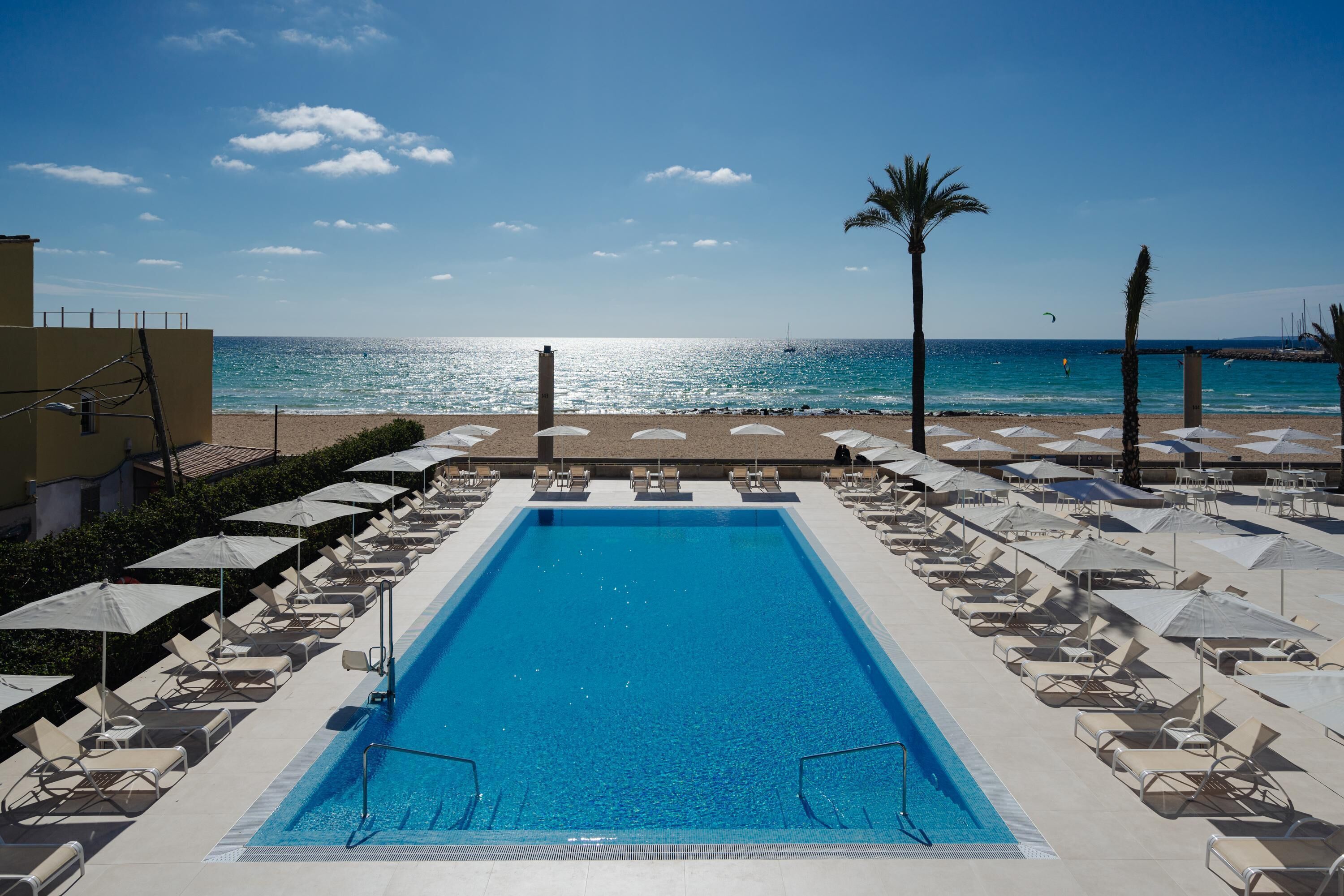 Zona de piscina con sillas de descanso y sombrillas, vista despejada a la playa y un mar tranquilo.