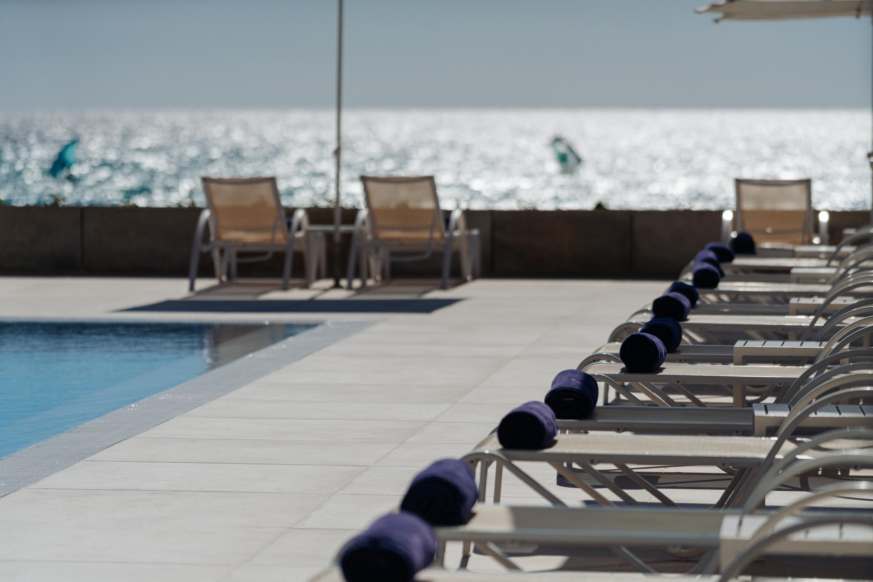 Zona junto a la piscina con tumbonas y vistas al mar.