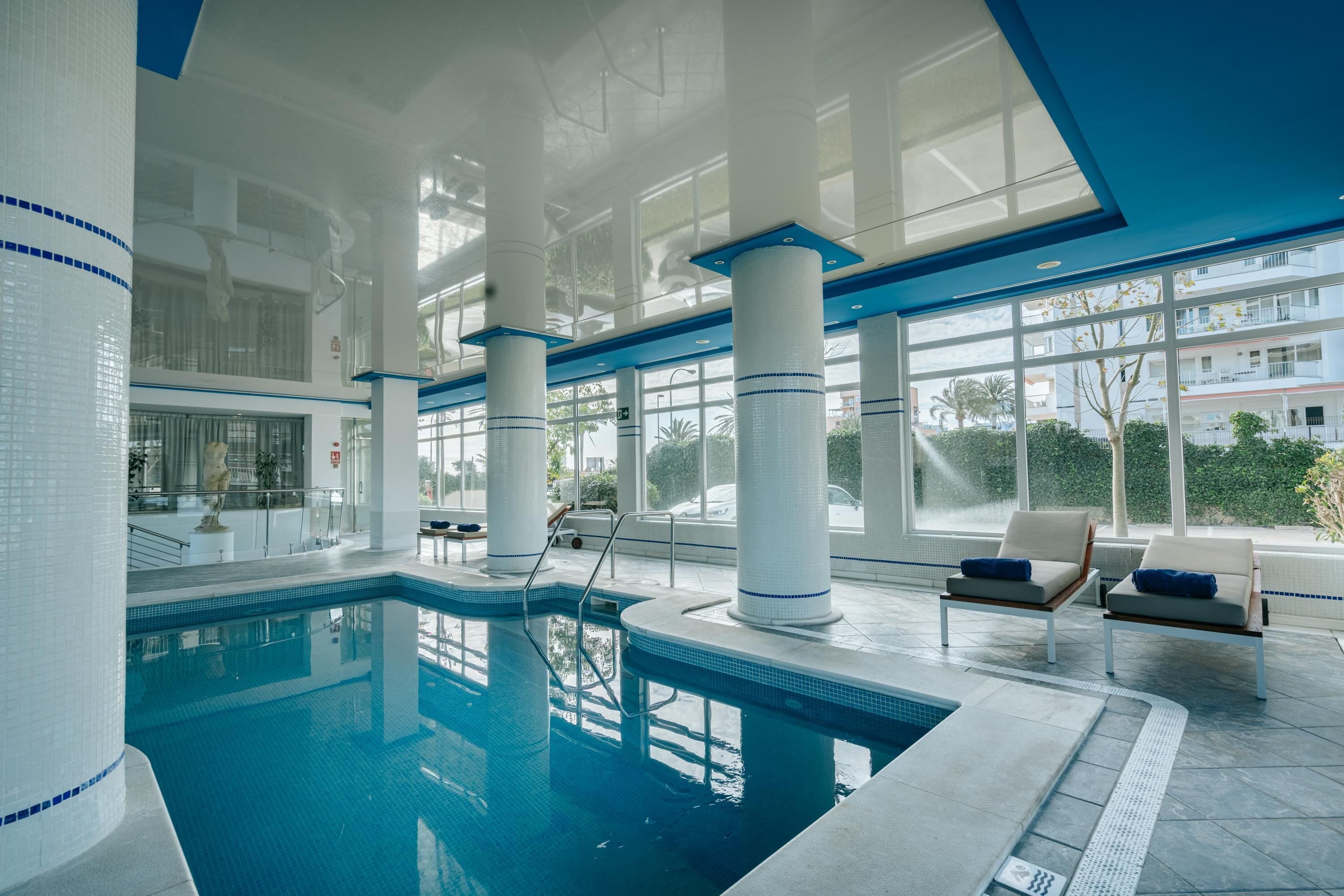 Una piscina interior con agua cristalina azul, grandes ventanales y arquitectura moderna.