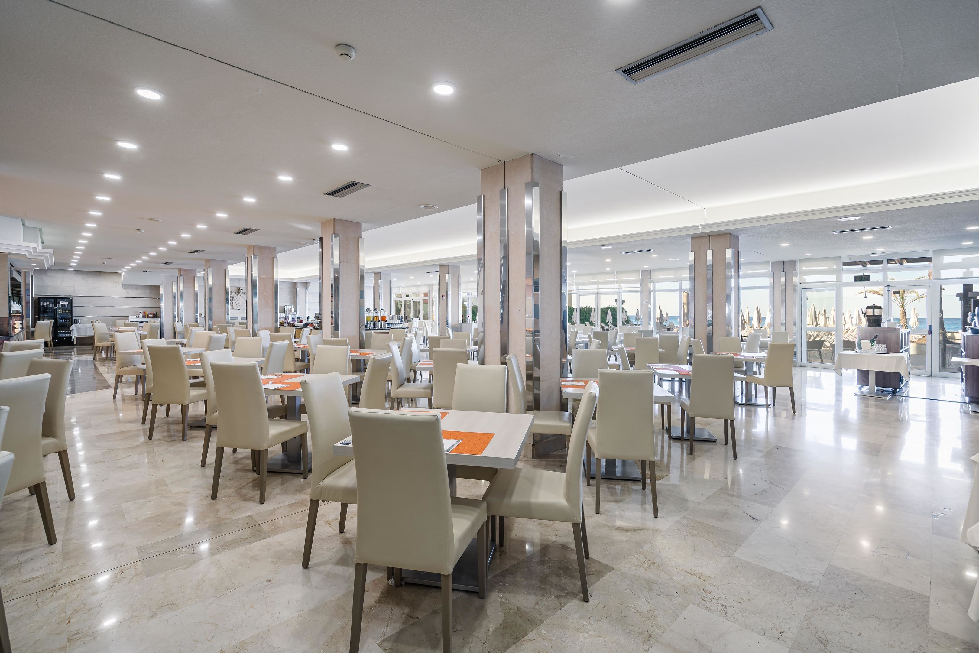 A spacious dining area with multiple tables and chairs, large pillars, and a modern ceiling design.