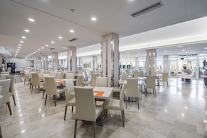 Un comedor espacioso con varias mesas y sillas, pilares grandes y un diseño de techo moderno.