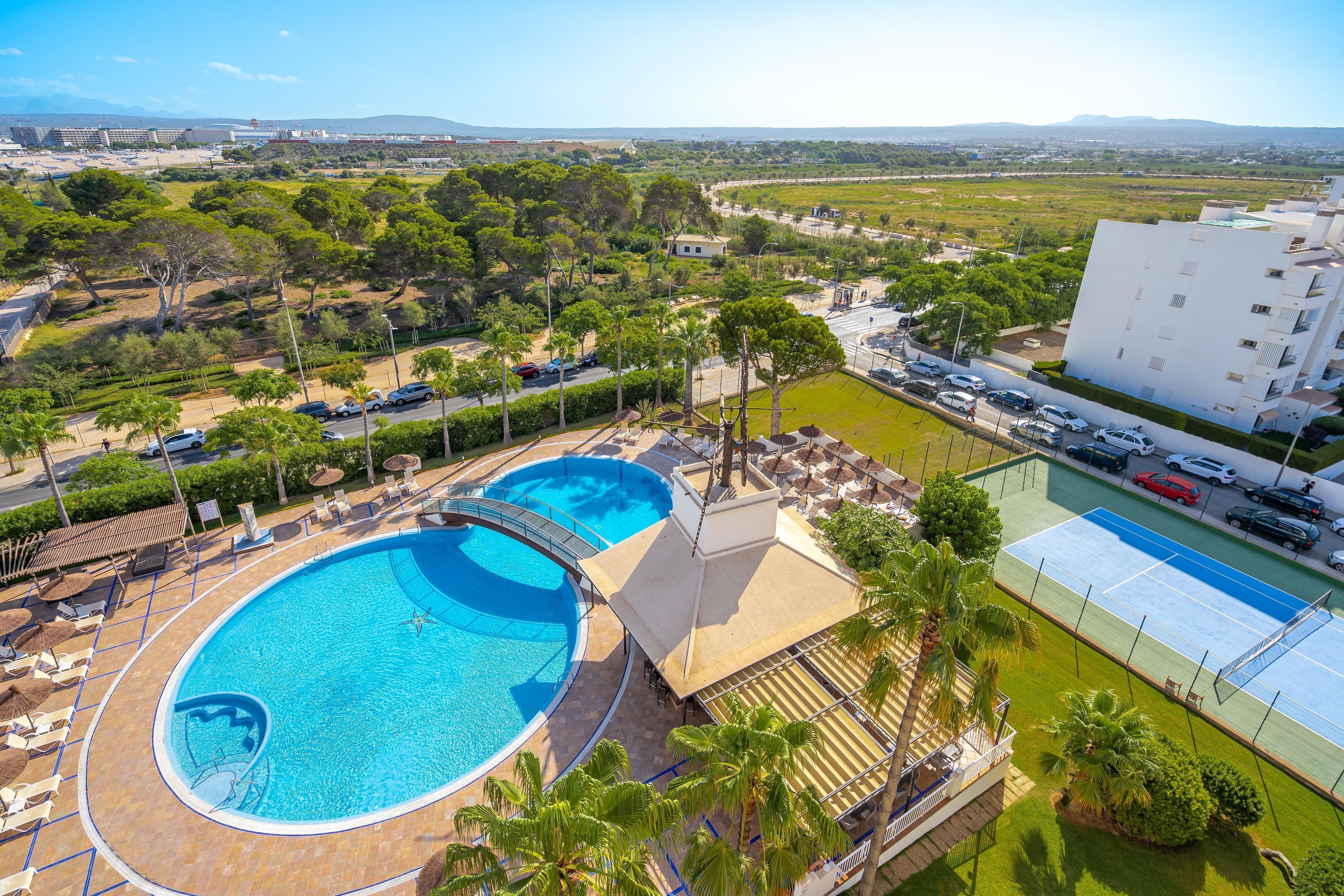 A resort with a large swimming pool, tennis court, and lush greenery.