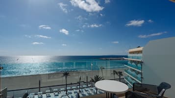 Un balcon avec vue sur la plage et l’océan, un espace piscine, ainsi qu’une table et des chaises.