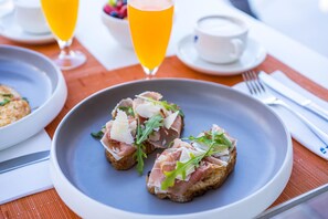 A plate of bruschetta with prosciutto and arugula on a table with a napkin and cutlery. - Hotel THB El Cid - Adults Only (Palma de Mallorca)