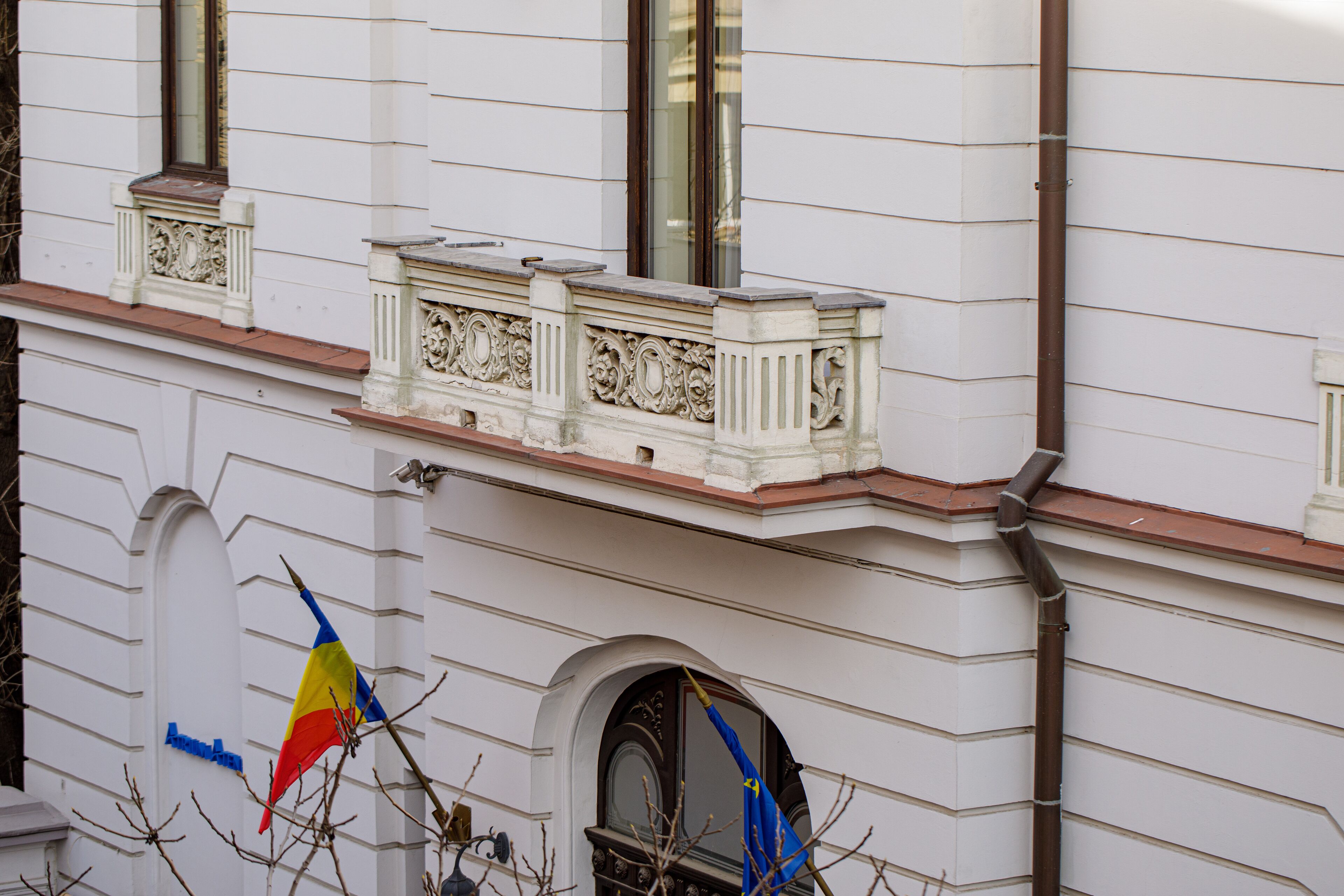 Fachada de edificio con paredes exteriores blancas, marcos de ventanas decorativos y borde de techo marrón.
