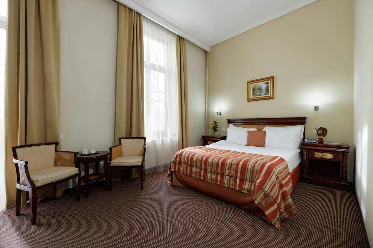 A hotel room with a large bed, two chairs, a small table, and a nightstand with a lamp.