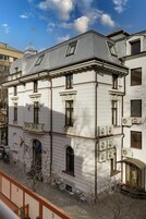 Un edificio blanco con numerosas ventanas y unidades de aire acondicionado, que cuenta con un balcón y un pequeño jardín.