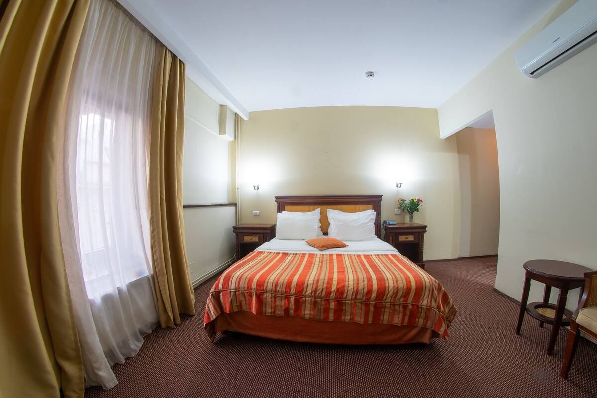 A hotel room with a large bed, a bedside table with a lamp, a small table, and a chair.