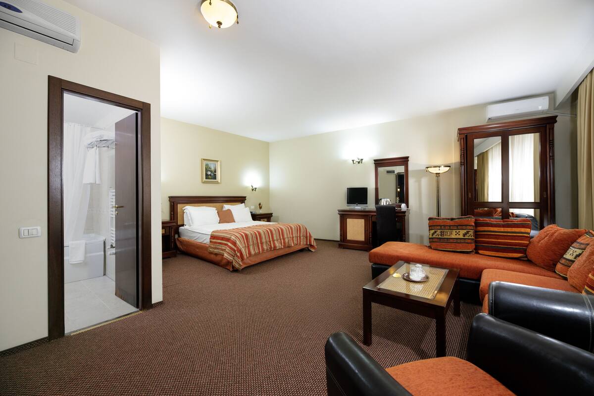 A hotel room with a bed, a sofa, a desk, and a mirror.