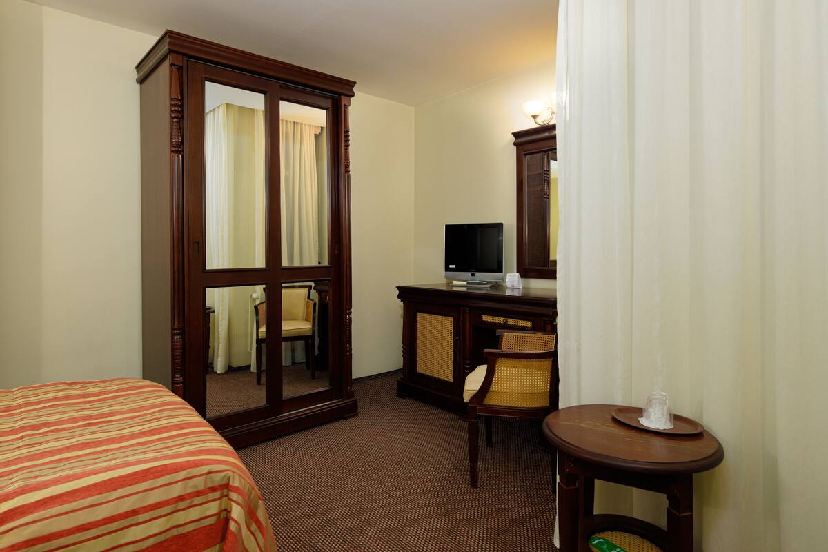 A hotel room with a bed, a desk with a television, a chair, and a small table with a decorative item.