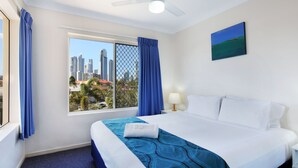 Habitación de hotel con una cama grande, una ventana con cortinas azules, vista a la ciudad y un ventilador de techo.
