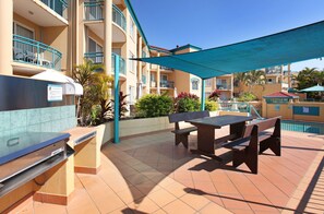 A patio area with a barbecue grill, outdoor seating, and a pool. - Paradise Isles (Surfers Paradise)