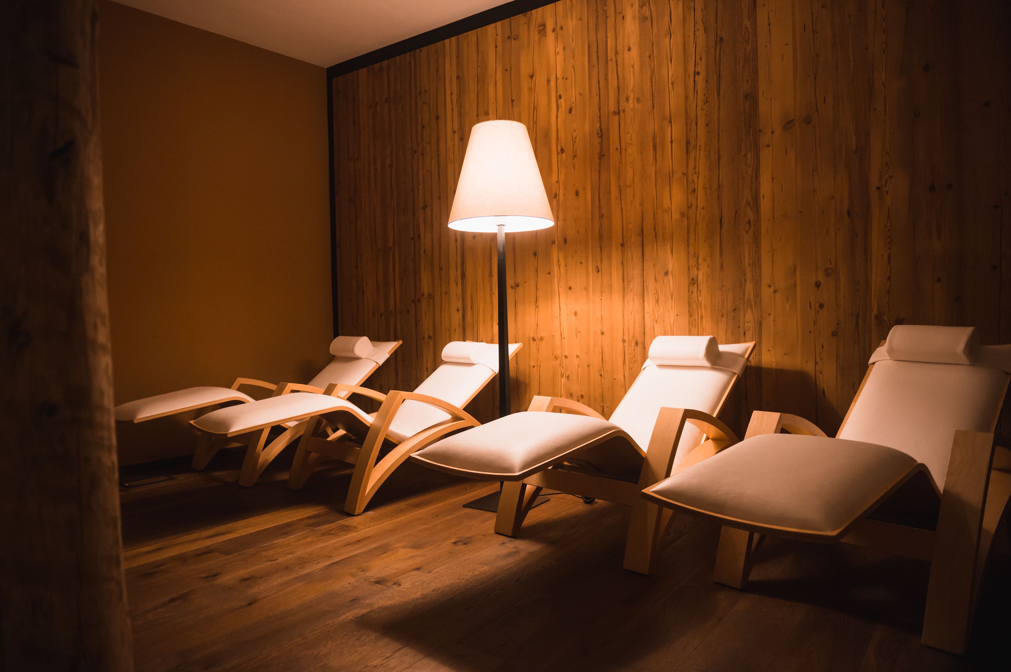 Ein Zimmer mit Holzwandverkleidung, einer Stehlampe und mehreren weißen Loungesesseln.