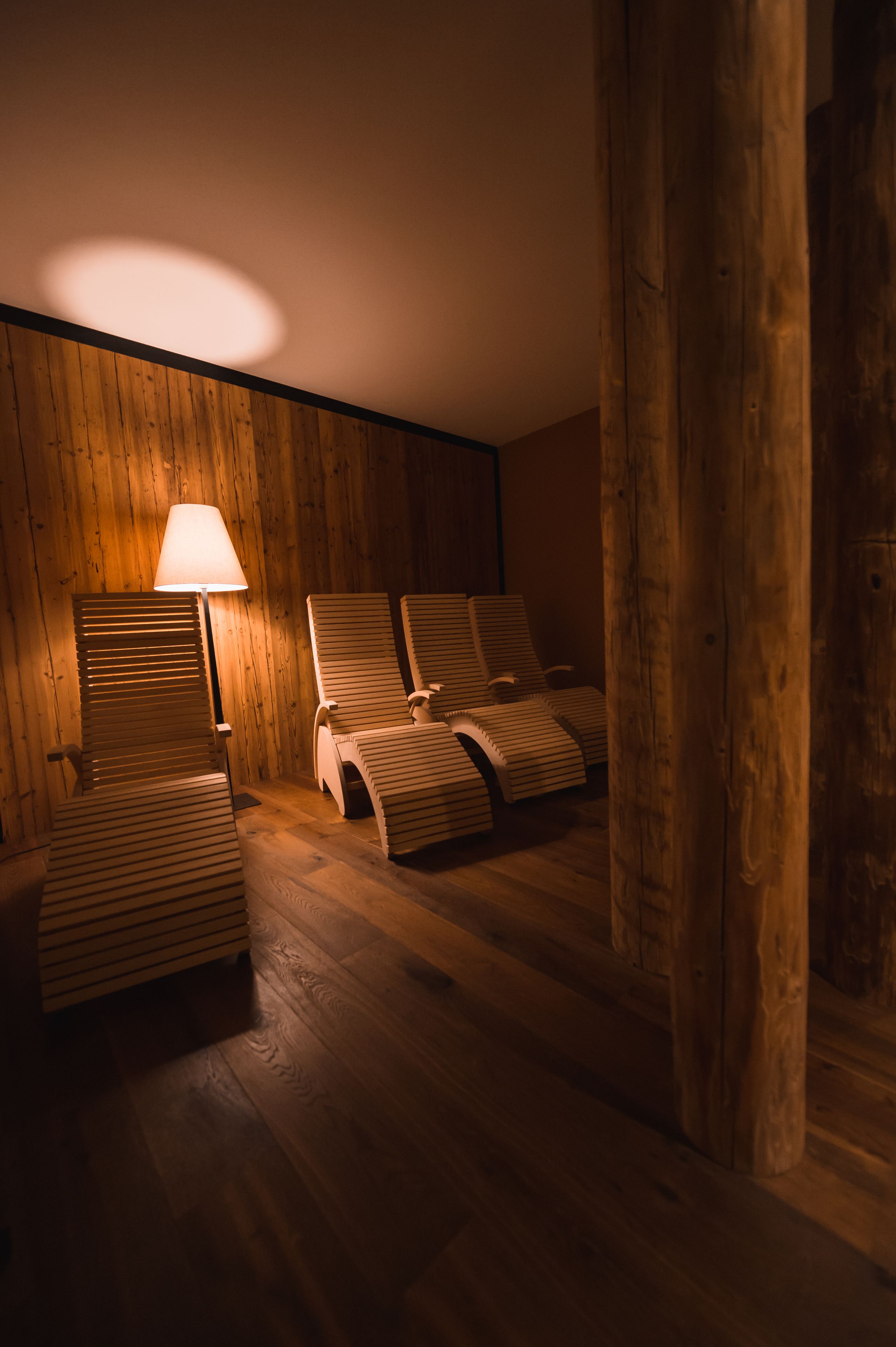 A room with wooden walls and floors, featuring three wooden chairs and a floor lamp.