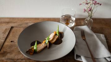 Un plato de comida sobre una mesa de madera, con un vaso de agua y un jarrón de flores al fondo.