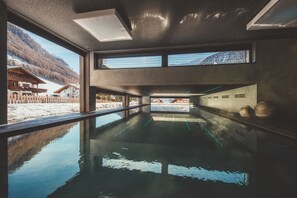 Une piscine intérieure moderne offrant une vue dégagée sur les montagnes enneigées et bordée d’un bâtiment en bois à l’extérieur.