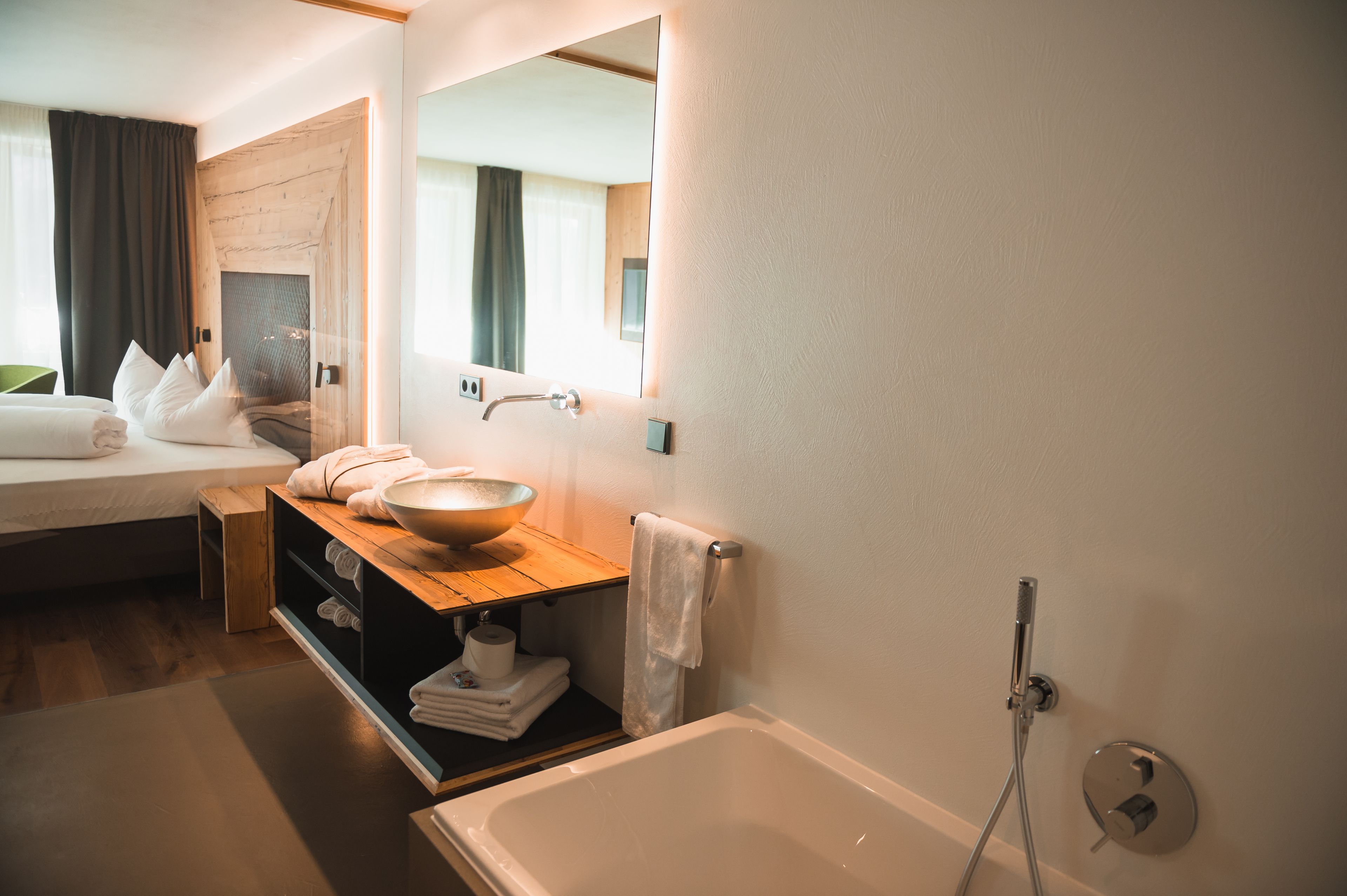 Una habitación de hotel moderna con una cama grande, un tocador de madera con lavabo y un espejo amplio, además de un área de ducha independiente.