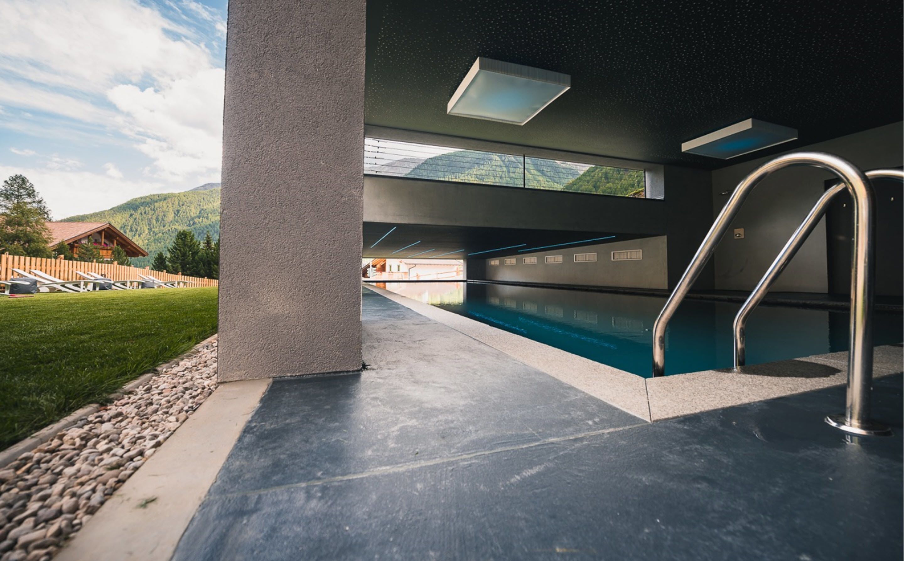 Una piscina interior con vistas despejadas a las montañas, suelo de hormigón y barandillas de metal.