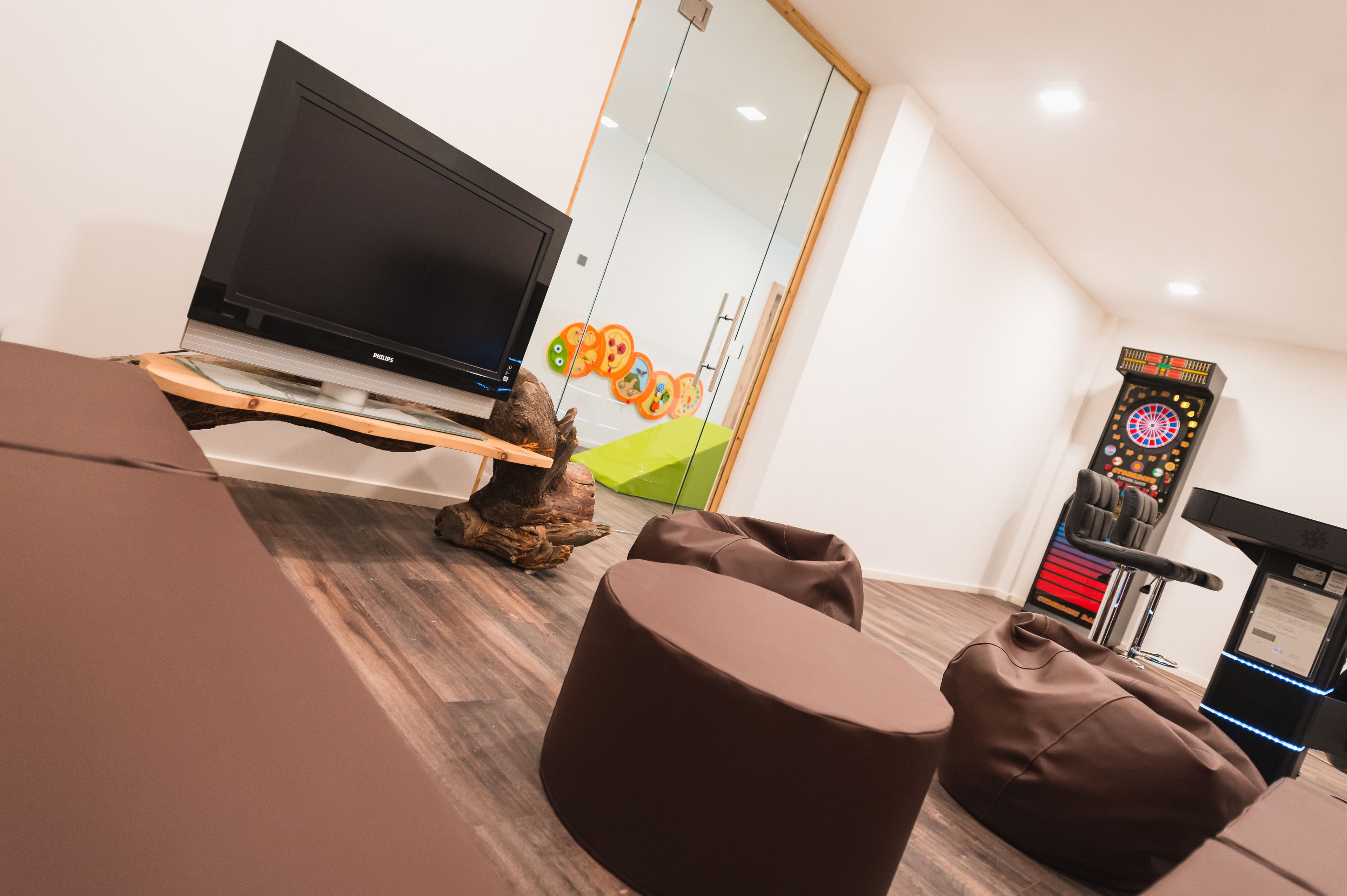 A modern living room with a flat-screen TV, bean bag chairs, a treadmill, and a wall with colorful artwork.